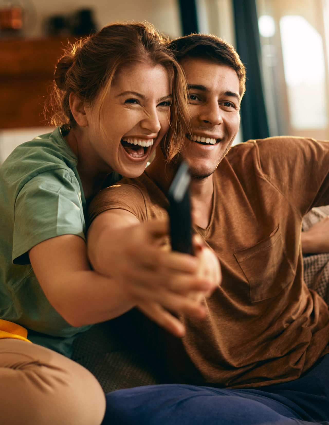 Young couple having fun while watching TV and struggling about remote controller at home.